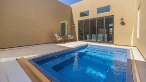 A swimming pool with a clear blue water, surrounded by a patio area with chairs.