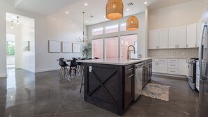 A modern kitchen with a large island, pendant lights, and white cabinetry.