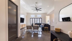 A spacious living area with a dark floor, a ceiling fan, a sofa, a coffee table, and a TV mounted on the wall.