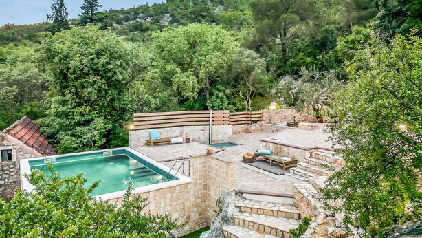 Zona de piscina con cubierta de piedra, un banco de madera y pared de piedra.