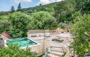 Relax by the pool surrounded by lush greenery and a stone patio.