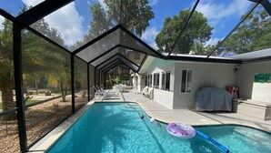 Una piscina con agua azul cristalina, rodeada por un porche cubierto con sillas de descanso y una zona de estar techada.