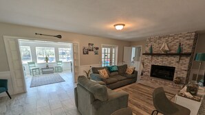 Amplia sala de estar con chimenea, un conjunto de sofás y un comedor con cocina al fondo.
