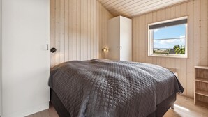 Een slaapkamer met een groot bed, houten wanden, een raam met uitzicht en een deur.