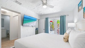Une chambre à coucher avec un lit, un ventilateur de plafond, une télévision et une vue sur l’extérieur.