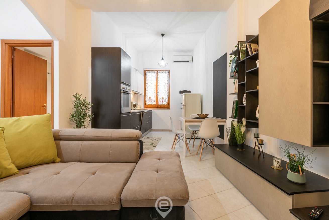 A modern living room with a sofa, a dining area, and a kitchen.