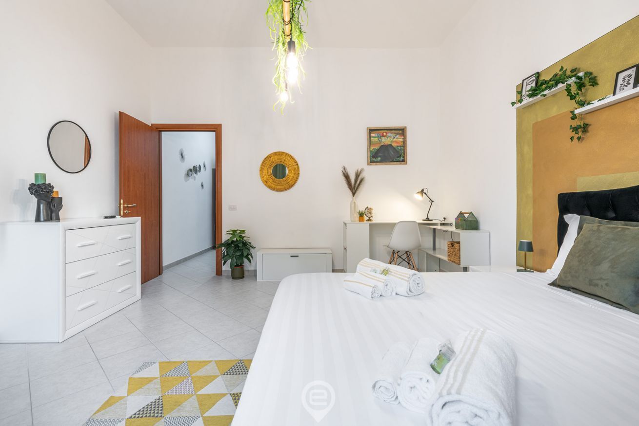 Moderni hotellihuone, jossa on sänky, työpöytä, tuoli, vaatekaappi ja kylpyhuone, joka näkyy avoimesta ovesta.