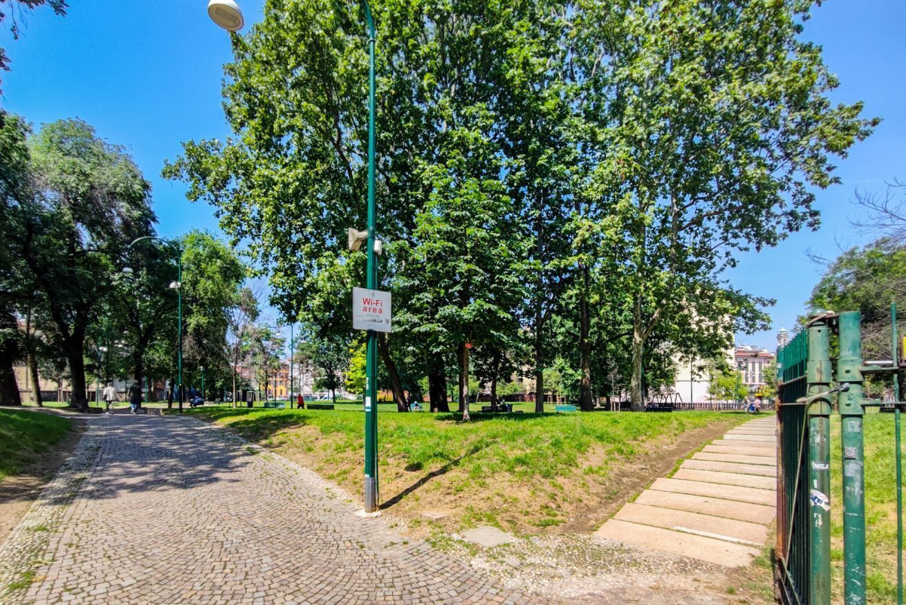 A paved pathway in a park with trees and a sign indicating a no-parking area.