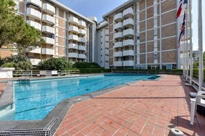 A swimming pool with a tiled deck, surrounded by a multi-story building with balconies.
