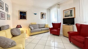 Un salon avec un canapé jaune, un canapé gris, un fauteuil rouge, un téléviseur et un meuble.