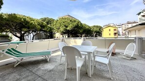 Une terrasse avec une table et des chaises, un fauteuil de relaxation et, au fond, un bâtiment jaune.