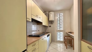 Une cuisine de taille réduite avec des meubles de couleur jaune, un lave-vaisselle et une fenêtre équipée de stores.
