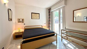 Une chambre à coucher avec un lit, des tables de chevet, un miroir et une fenêtre avec des rideaux.