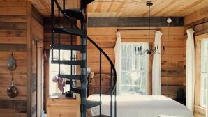 A cabin interior with a spiral staircase, wooden walls, a bed, a sofa, and a window with curtains. - Your 15 acres of privacy on the water- Rock Island (Rock Island)