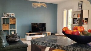 A modern living room with a television, a bowl of fruit, a sofa, and a bookshelf.