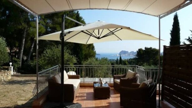 A covered outdoor seating area with a view of the sea, furnished with sofas and a table.