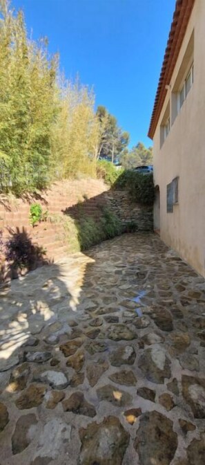 Pathway leads to a charming building with a red-tiled roof, surrounded by lush vegetation and a stone wall.