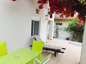 Eine kleine Terrasse im Freien mit Tisch, Stühlen und einer Bank, sowie ein Fenster.