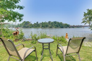 Angolo relax con sedute e tavolino sul lago, immerso nel verde e con vista su un ponte in lontananza.