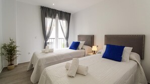Habitación de hotel con dos camas, una planta en maceta y una ventana con cortinas.