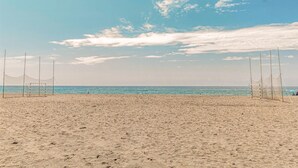 Playa con red y porterías de voleibol, cielo despejado y mar tranquilo.