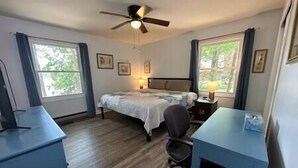 Une chambre à coucher comprenant un lit, un bureau, une chaise, un ventilateur de plafond et des fenêtres.