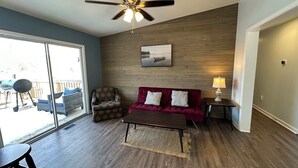 Un salon avec un canapé rouge, un plancher en bois, un ventilateur de plafond et une grande fenêtre.