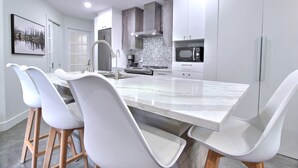 A modern kitchen with a large island, white chairs, and stainless steel appliances. - Peaceful Mountain Side Appartment Fully Equiped and Close to Many Activities (Bromont)