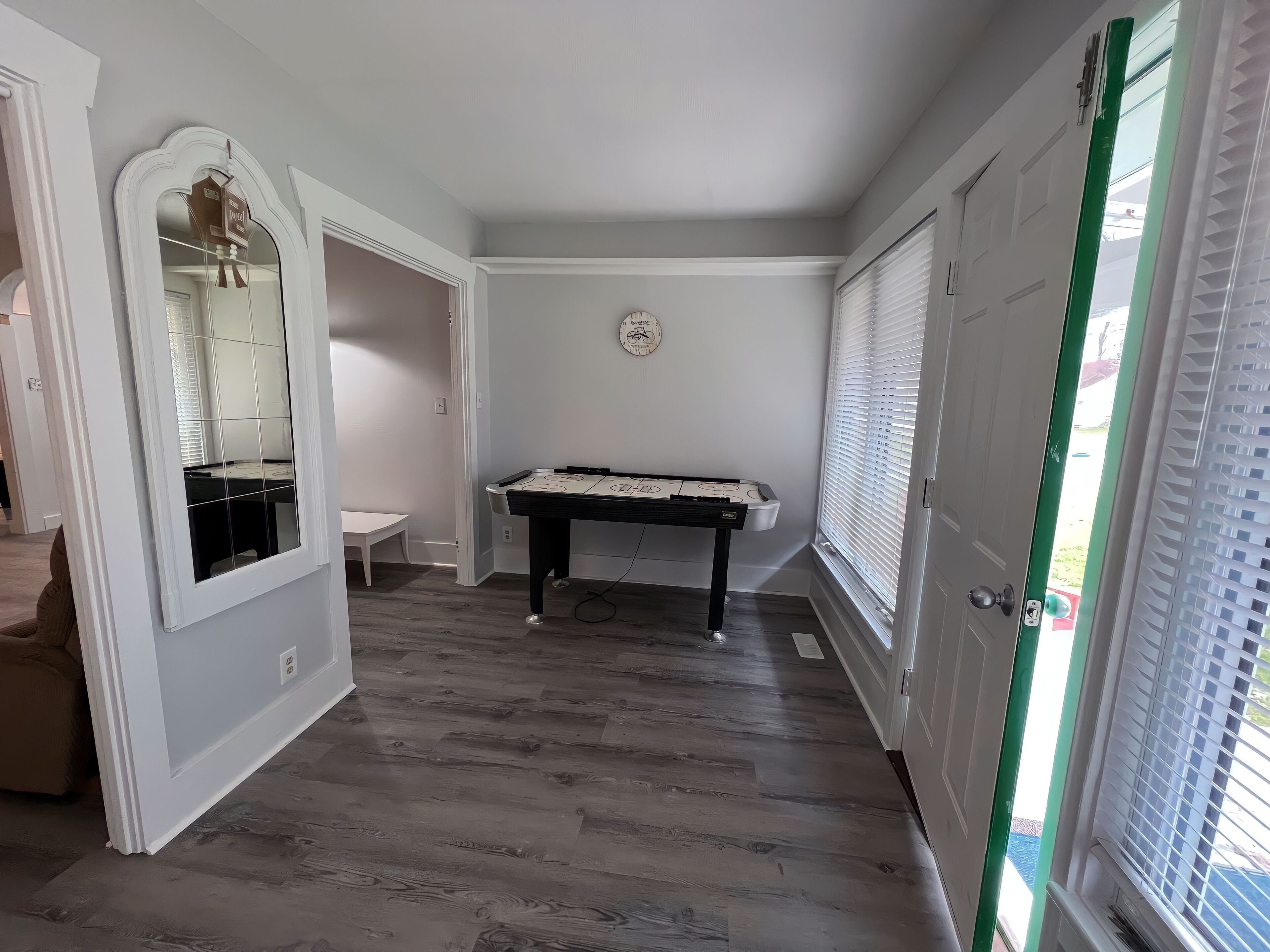 Un pasillo con una mesa de billar, un espejo y una puerta que da al exterior.