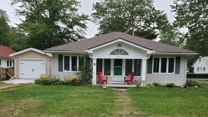 A single-story house with a porch, two red Adirondack chairs, and a garage. - Crystal Beach Getaway (Fort Erie)