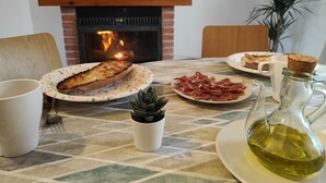 Een eettafel met borden eten, een karaf olijfolie en een haard op de achtergrond.