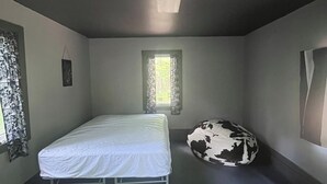 A bedroom with a single bed, a window with curtains, a round bean bag, and a ceiling light. - Mini Cabin Paradise -15 individual cabins with Access to Private Lake (Lake)