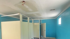 A room with blue walls, a tiled floor, and a white ceiling. There are three white partitions and a window on the right wall. - Mini Cabin Paradise -15 individual cabins with Access to Private Lake (Lake)