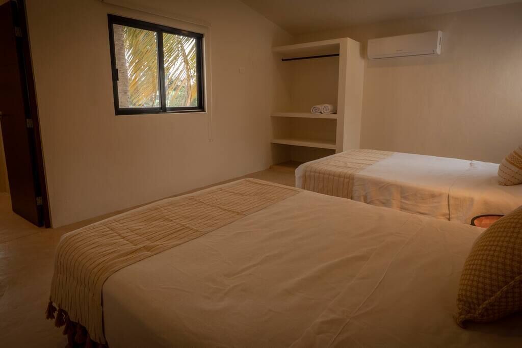 A room with two beds, a window, a wardrobe, and an air conditioning unit.