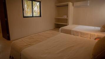 A room with two beds, a window, a wardrobe, and an air conditioning unit.