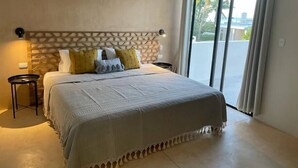 Een slaapkamer met een groot bed, een hoofdbord met een geometrisch patroon en uitzicht op een balkon met gordijnen.