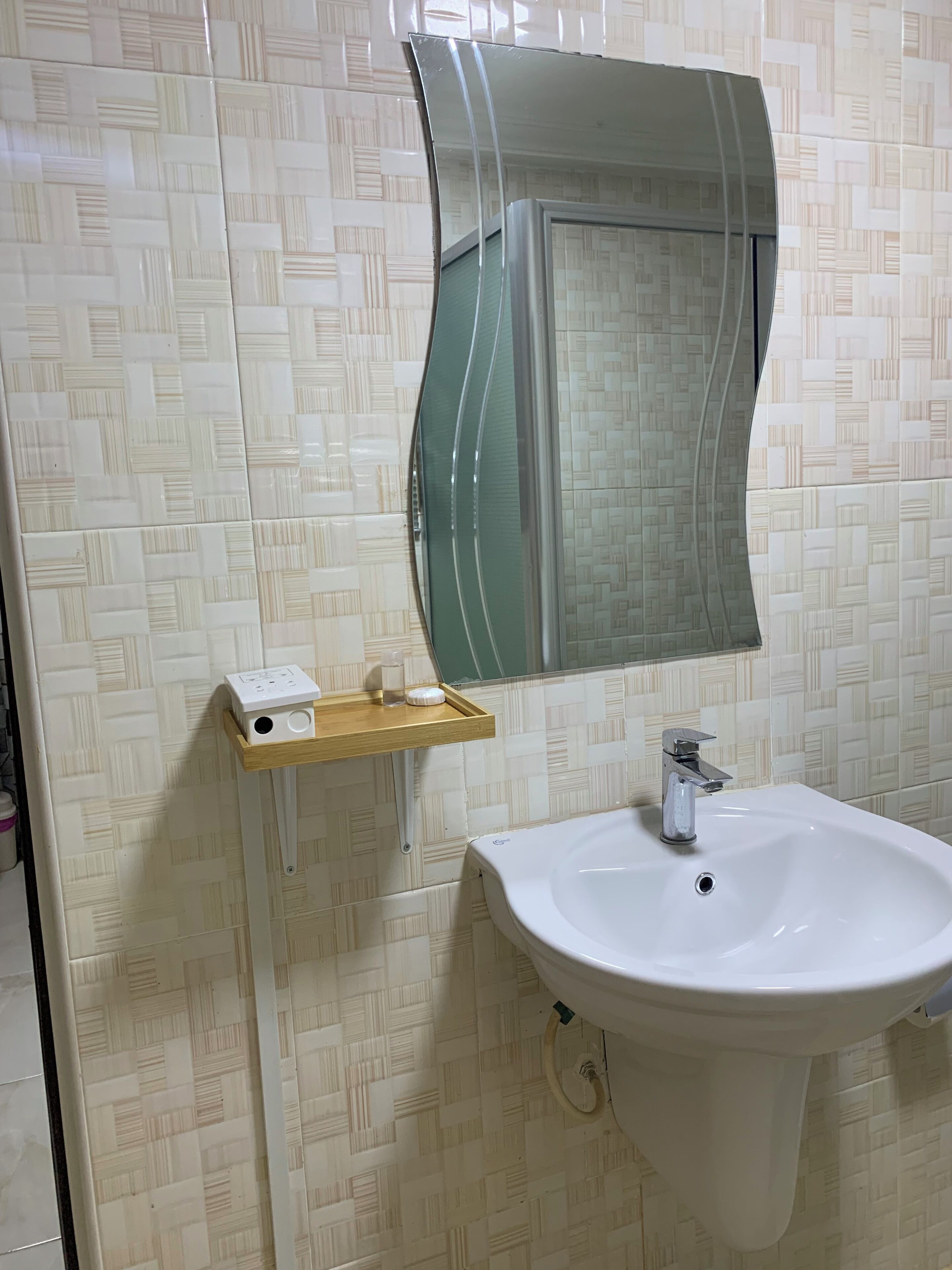 A bathroom with a white sink, a mirror with a curved frame, and a wooden shelf with a power outlet.