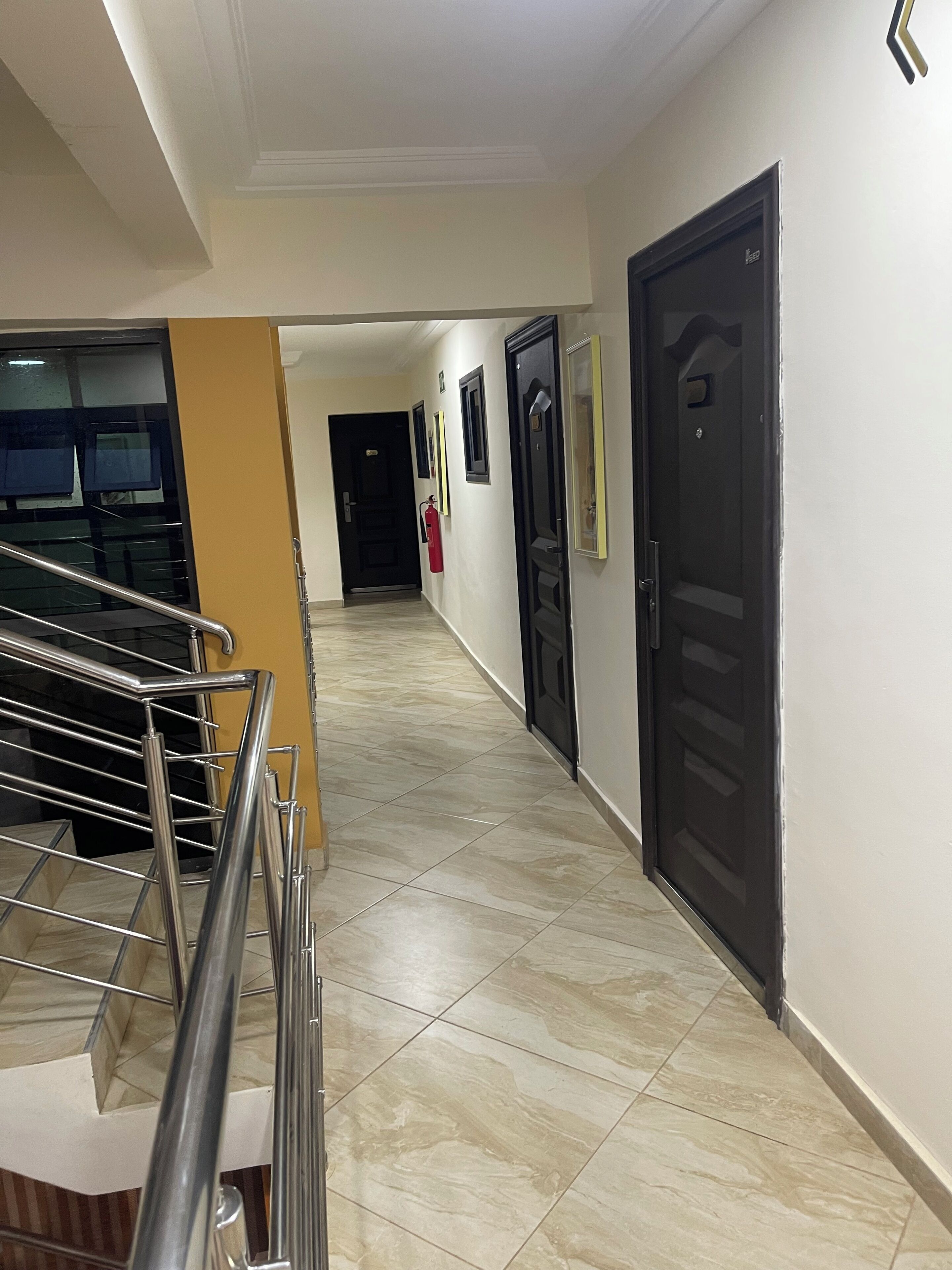 A corridor with a staircase on the left, a fire extinguisher on the wall, and a door at the end.