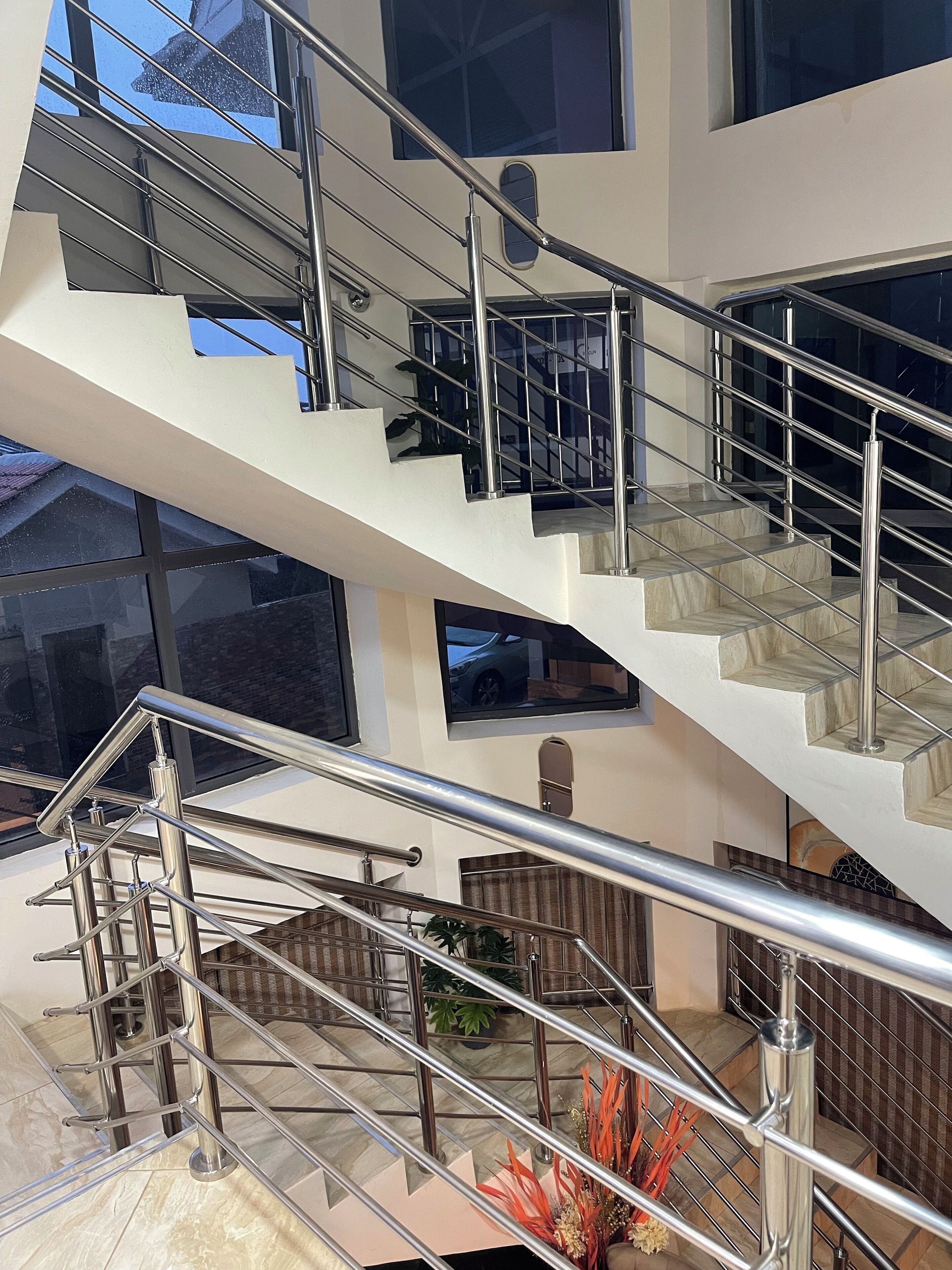 A multi-level interior with modern metal railings and glass railings, featuring a spacious atrium with plants and seating areas.
