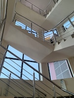 Interior com vários níveis, grades de metal e grandes janelas que permitem entrada de luz natural.