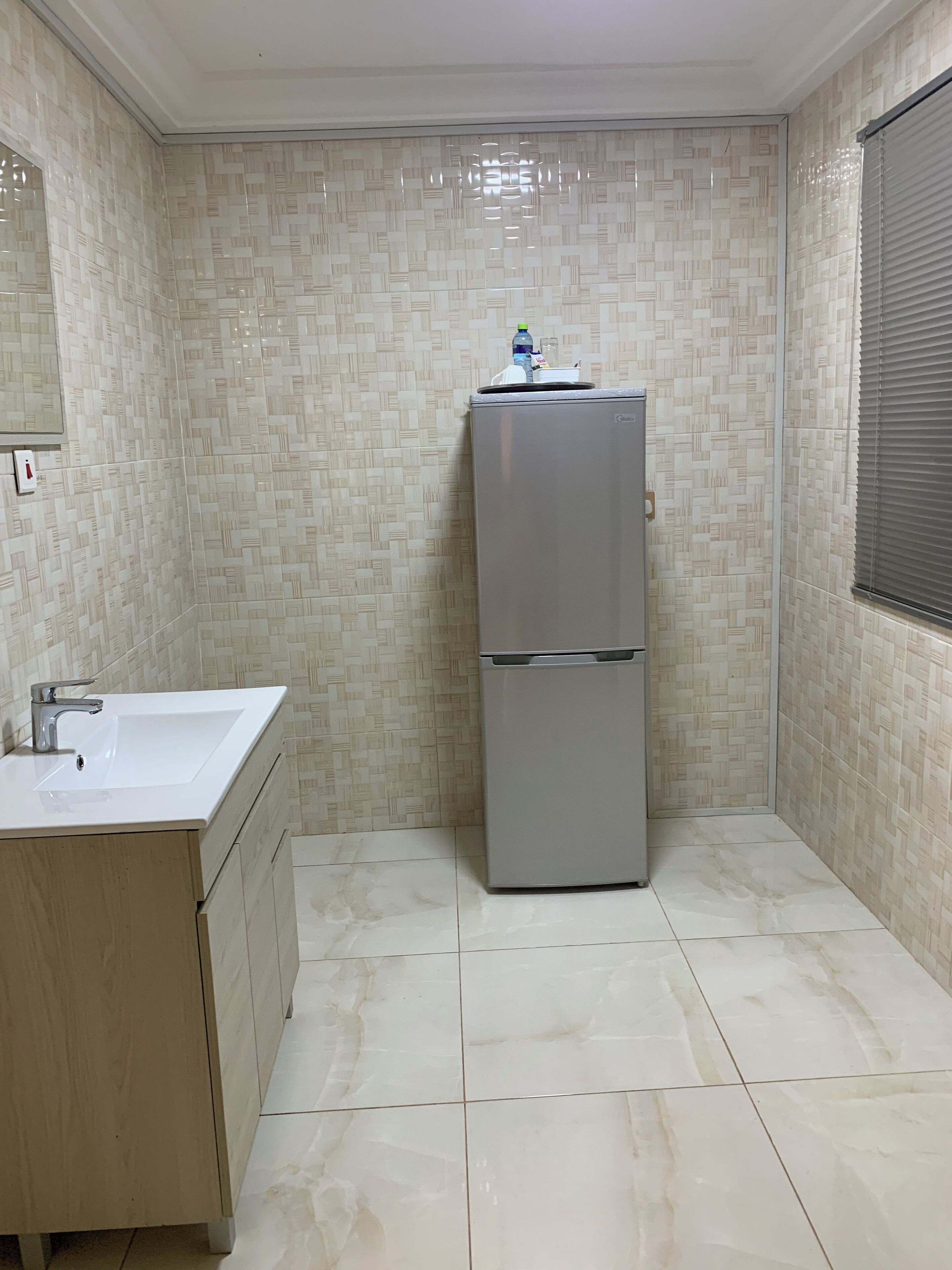 Un baño pequeño y limpio con lavamanos, espejo y un refrigerador de doble puerta.