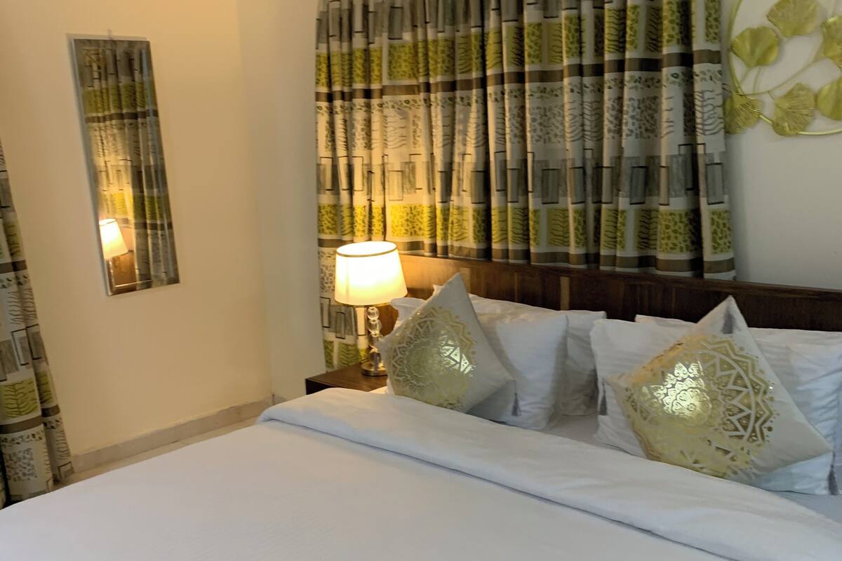 A neatly made bed with white linens and decorative pillows, a bedside lamp, and a wall-mounted mirror.