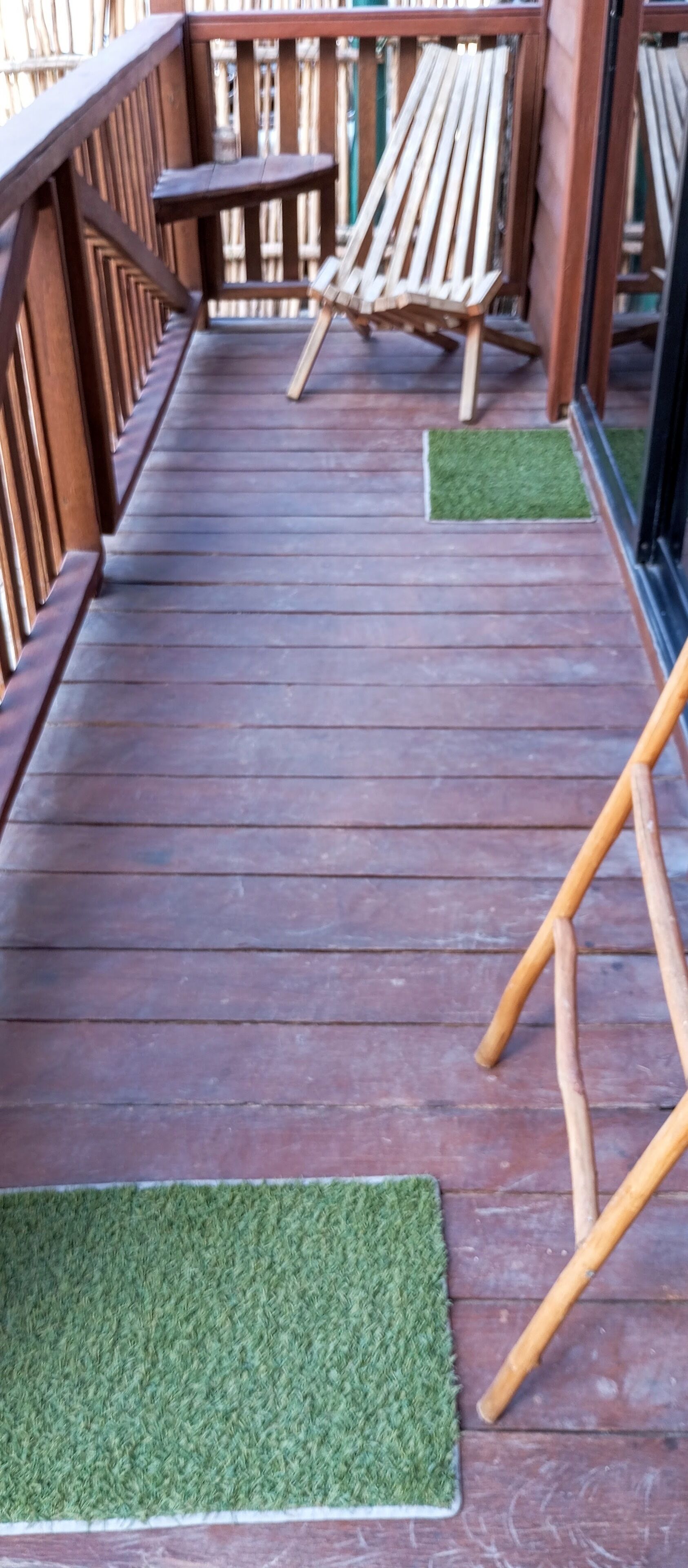 Une terrasse en bois avec une rambarde, deux chaises en bois et une petite table.