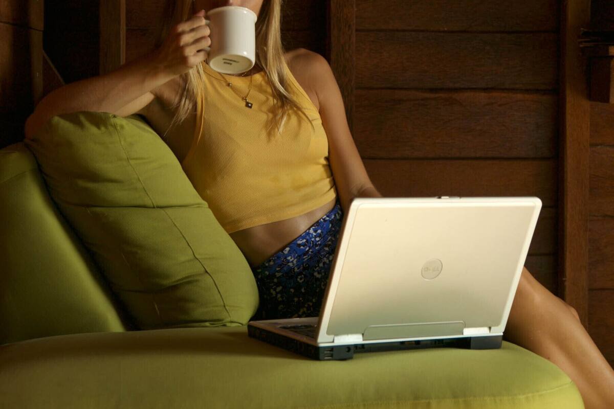 Een persoon zit op een groene bank met een laptop voor zich.