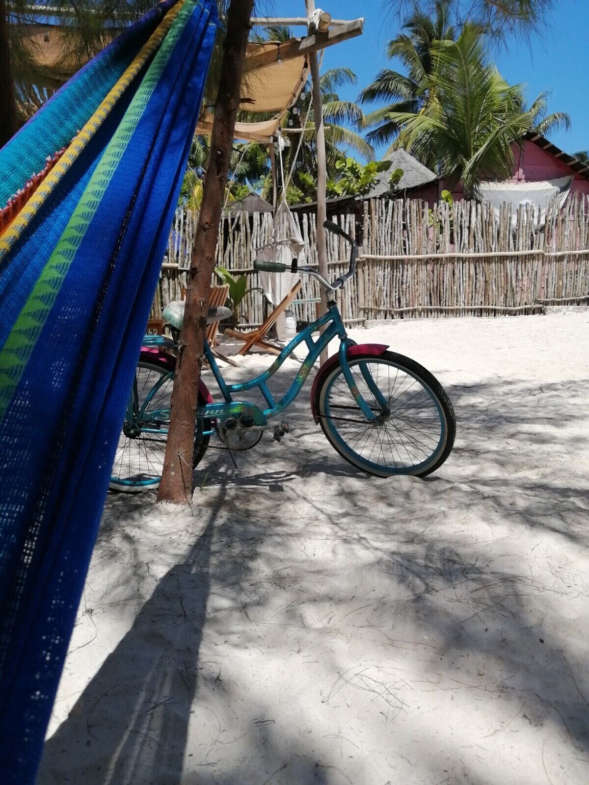 Una hamaca, una bicicleta y una valla de madera en un entorno soleado al aire libre.