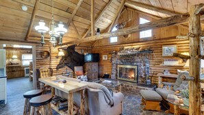 Interno di un rustico rifugio con camino in pietra, mobili in legno e testa di cervo appesa al muro.