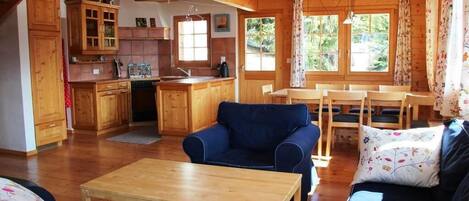A cozy cabin interior with wooden floors, a dining area, a kitchen with wooden cabinets, and a living room with a sofa and a coffee table.
