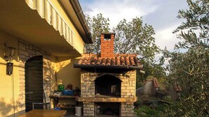 Eine Außenpatio-Terrasse mit einem gemauerten Pizzaofen, Holzbanken und einem gefliesten Boden.