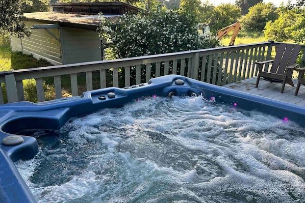 A hot tub with water jets, surrounded by a wooden deck and a chair.
