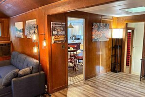 A wooden interior with a sofa, a dining area, and a kitchen visible through an open door.